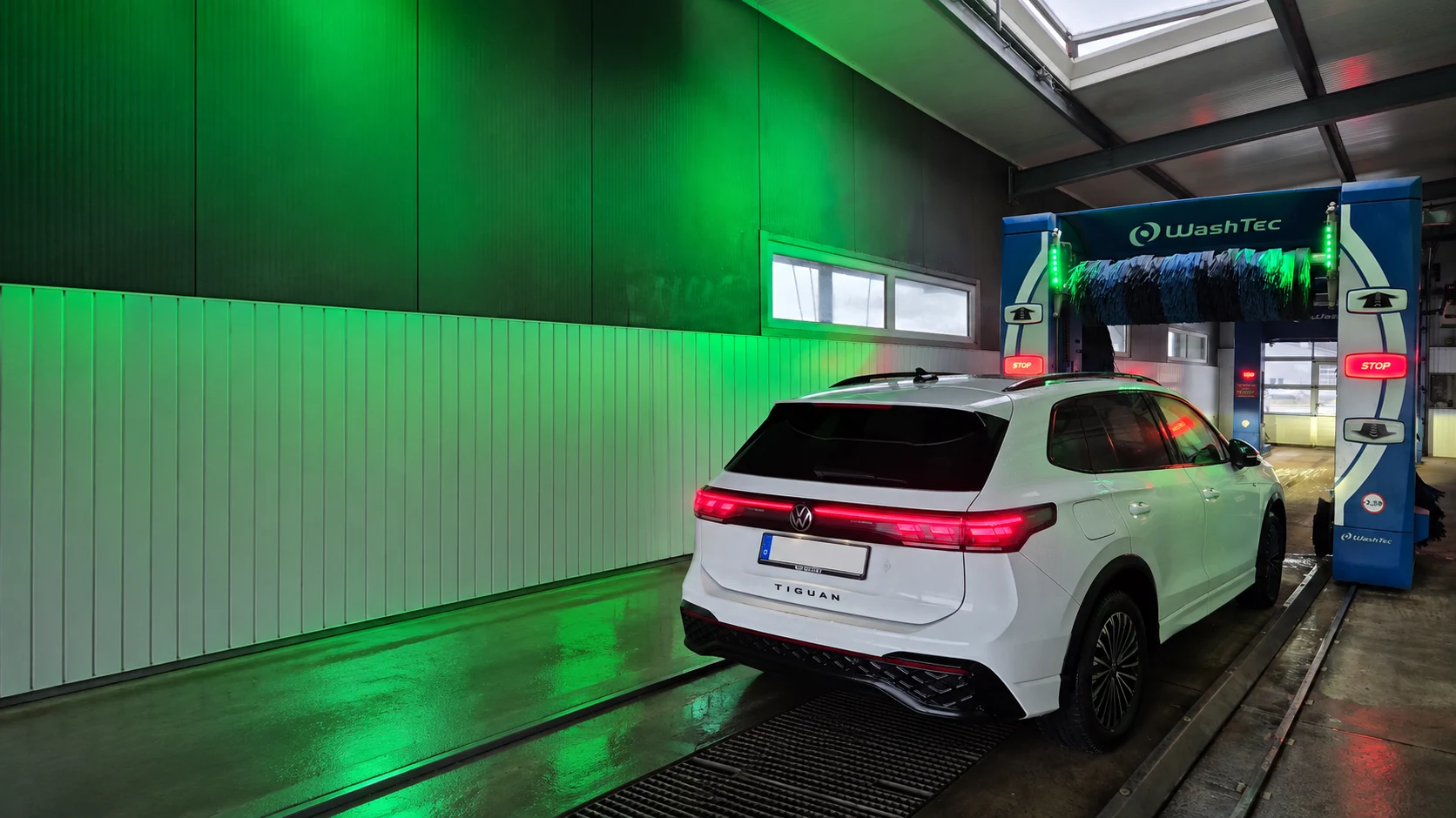 Weißer VW Tiguan vor der blau-grün beleuchteten WashTec-Portalanlage; das Kennzeichen ist unkenntlich
